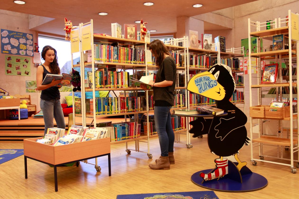 Zwei Leserinnen stehen vor den Bücherregalen und blättern in Büchern